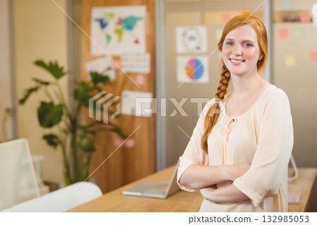 Red-haired woman in her 20s standing at office table with laptop and corkboard map, copy space 132985053