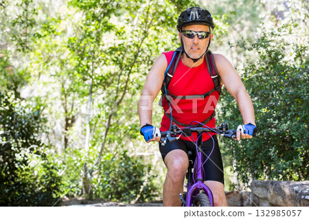 Male cyclist riding purple mountain bike on wooded trail wearing red top and hydration pack Male cyclist riding purple mountain bike on wooded trail wearing red top and hydration pack 132985057
