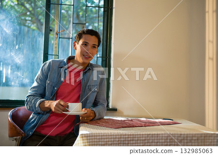 Adult Asian man in denim jacket holding ceramic cup and saucer in dining area, copy space Adult Asian man in denim jacket holding ceramic cup and saucer in dining area, copy space 132985063