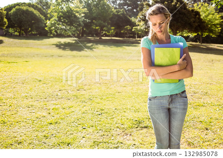 Female student standing holding colorful binders in sunny grassy park with tree shadows, copy space Female student standing holding colorful binders in sunny grassy park with tree shadows, copy space 132985078
