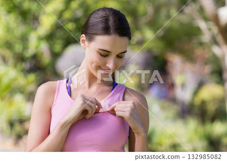 Woman adjusting pink athletic tank top over blue sports bra in garden under bright sunlight 132985082