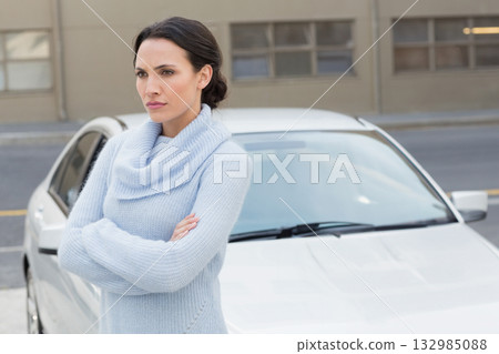Woman standing with arms crossed wearing knit sweater on urban sidewalk in front of parked sedan 132985088