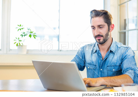 Man typing on silver laptop at wooden desk in bright office with potted plant, copy space Man typing on silver laptop at wooden desk in bright office with potted plant, copy space 132985104