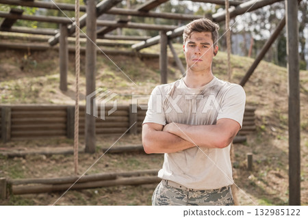 Male military trainee standing on wooden obstacle course wearing camo pants, muddy shirt and earbud Male military trainee standing on wooden obstacle course wearing camo pants, muddy shirt and earbud 132985122