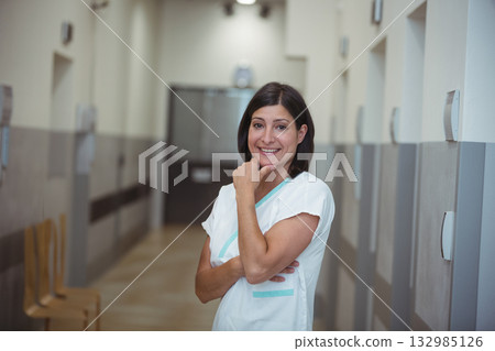 Female nurse standing and smiling in hospital corridor with wooden chairs and double doors Female nurse standing and smiling in hospital corridor with wooden chairs and double doors 132985126
