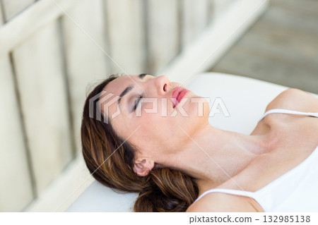 Woman lying on cushioned treatment table on spa deck wearing camisole using pillow near railing Woman lying on cushioned treatment table on spa deck wearing camisole using pillow near railing 132985138