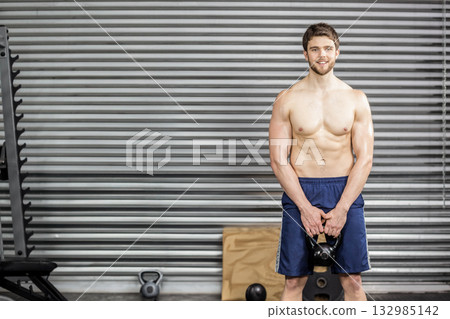 Man gripping kettlebell at thigh level in gym with weight rack, plyometric box, copy space Man gripping kettlebell at thigh level in gym with weight rack, plyometric box, copy space 132985142
