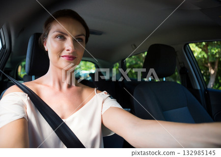 Female driver wearing seatbelt and gripping steering wheel while driving on sunny tree-lined road Female driver wearing seatbelt and gripping steering wheel while driving on sunny tree-lined road 132985145
