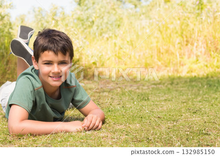Child boy lying on stomach in sunny open meadow surrounded by tall grass, copy space 132985150