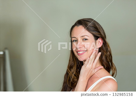 Woman standing in studio against pale wall touching cheek with fingertips, copy space 132985158