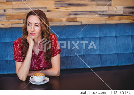 Woman wearing red polka-dot blouse sitting at cafe table gazing at latte art cup, copy space 132985172