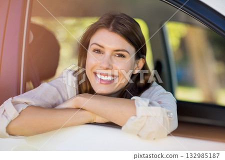 Woman leaning out car window wearing light-colored shirt on sunny suburban street by white car door 132985187