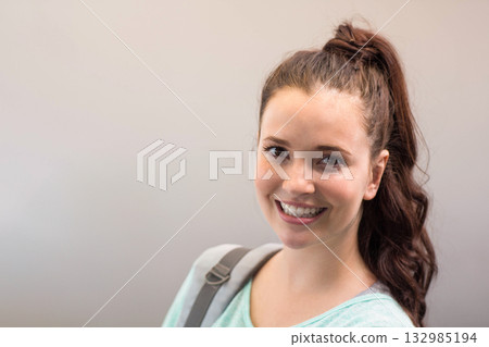 Female student standing in hallway wearing mint green top and gray backpack strap, copy space 132985194
