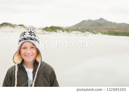 Smiling child boy standing on sandy shore wearing olive green jacket and ear-flap hat, copy space Smiling child boy standing on sandy shore wearing olive green jacket and ear-flap hat, copy space 132985203