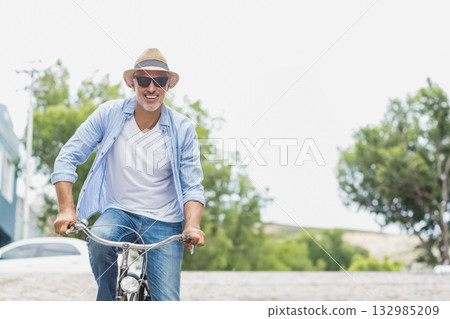 Middle-aged male riding bicycle on suburban street wearing straw hat and sunglasses with parked car Middle-aged male riding bicycle on suburban street wearing straw hat and sunglasses with parked car 132985209