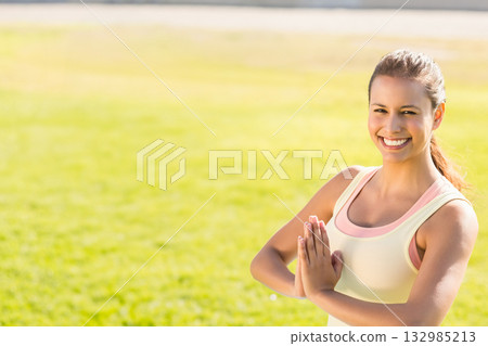 Female practicing yoga pose wearing pale yellow tank top, peach sports bra at park, copy space 132985213