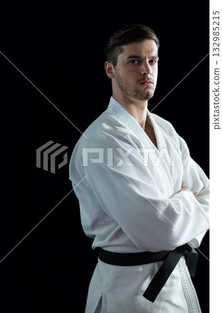 Male martial artist wearing white gi, black belt in studio against black backdrop looking serious 132985215