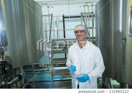 Male technician in protective gear inspecting tanks in processing plant using clipboard and pen Male technician in protective gear inspecting tanks in processing plant using clipboard and pen 132985222