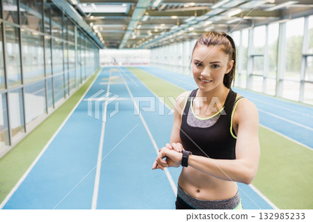 Athletic woman in sportswear checking smartwatch on right track in hall by glass wall, copy space 132985233