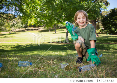 Boy wearing green gloves kneeling and picking up bottles and glass jar at park, copy space 132985238
