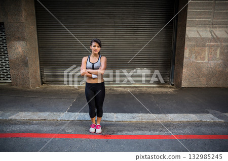 Japanese woman standing arms crossed on street by roll-up shutter, wearing sportswear and sweatband Japanese woman standing arms crossed on street by roll-up shutter, wearing sportswear and sweatband 132985245