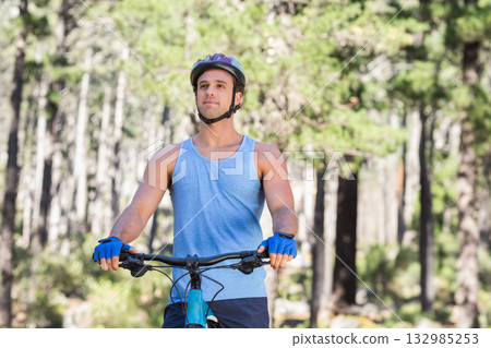 Man standing on pine forest trail wearing cycling helmet beside mountain bicycle under sunlight Man standing on pine forest trail wearing cycling helmet beside mountain bicycle under sunlight 132985253