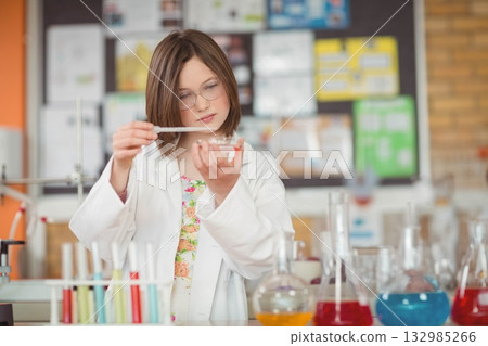 Girl wearing lab coat and safety glasses transferring with pipette into Petri dish in school lab Girl wearing lab coat and safety glasses transferring with pipette into Petri dish in school lab 132985266