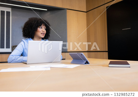 African American woman in blue blouse reviewing papers on laptop at meeting table, copy space African American woman in blue blouse reviewing papers on laptop at meeting table, copy space 132985272