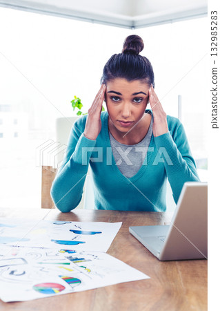 Woman working on laptop at wooden desk in bright office space, reviewing colorful charts 132985283