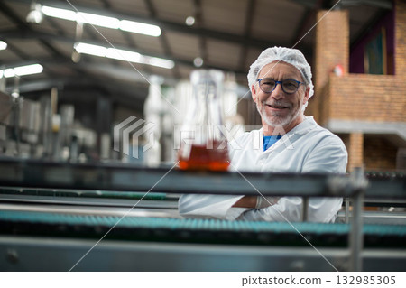 Senior man wearing lab coat inspecting Erlenmeyer flask on conveyor belt in plant, copy space Senior man wearing lab coat inspecting Erlenmeyer flask on conveyor belt in plant, copy space 132985305