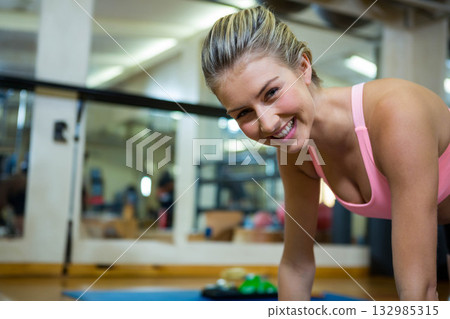 Woman holding plank wearing pink top, leggings on blue mat in studio mirrored wall, copy space Woman holding plank wearing pink top, leggings on blue mat in studio mirrored wall, copy space 132985315