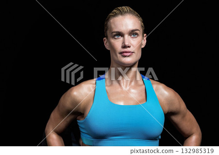 Fit woman standing confidently in studio wearing bright blue sports bra on black backdrop Fit woman standing confidently in studio wearing bright blue sports bra on black backdrop 132985319