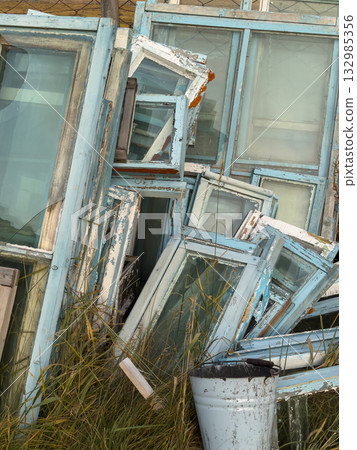 Piles of Old Blue Window Frames Stacked in a Grassy Yard with Rust and Glass Piles of Old Blue Window Frames Stacked in a Grassy Yard with Rust and Glass 132985356