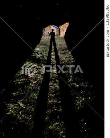Silhouette of person standing in dark tunnel with backlit barns at night 132985360