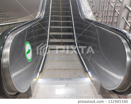 Bottom-up view of automatic escalator captured from lower level showing ascending metal steps and mechanical structure at night in public space or station Bottom-up view of automatic escalator captured from lower level showing ascending metal steps and mechanical structure at night in public space or station 132985380