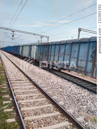 Freight train with blue open wagons parked on railway track during daylight, captured from side angle 132985392