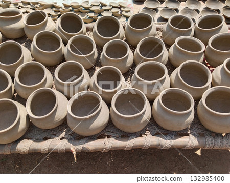 Clay pots placed in a line on a traditional charpai (village cot) for sun drying, showcasing rural pottery practices and preparation before storage or further processing in sunlight 132985400