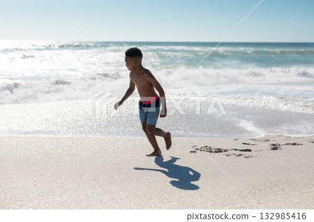 African American boy running along wet sand shoreline with ocean waves and striped swim trunks African American boy running along wet sand shoreline with ocean waves and striped swim trunks 132985416