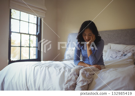 Senior Asian woman sitting on bed edge in softly lit bedroom, wearing pajama pants near window Senior Asian woman sitting on bed edge in softly lit bedroom, wearing pajama pants near window 132985419