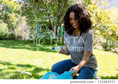 African American woman collecting litter in volunteer tshirt with bottle in park, copy space African American woman collecting litter in volunteer tshirt with bottle in park, copy space 132985431