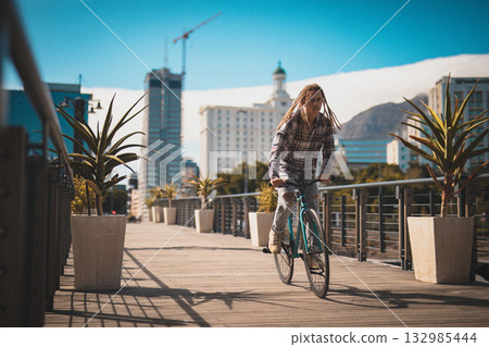Male in his twenties with long dreadlocks riding single-speed bike along boardwalk past planters Male in his twenties with long dreadlocks riding single-speed bike along boardwalk past planters 132985444