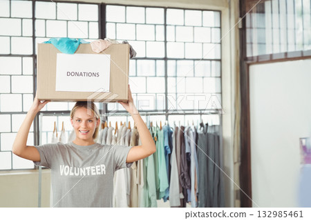 Female volunteer balancing Donations box on head while sorting garments on rack in sorting room Female volunteer balancing Donations box on head while sorting garments on rack in sorting room 132985461