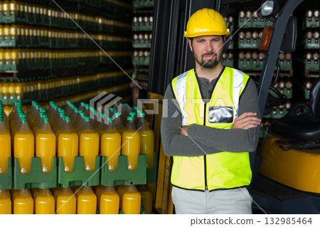 Male worker leaning against forklift wearing reflective vest in depot with juice crates, copy space Male worker leaning against forklift wearing reflective vest in depot with juice crates, copy space 132985464