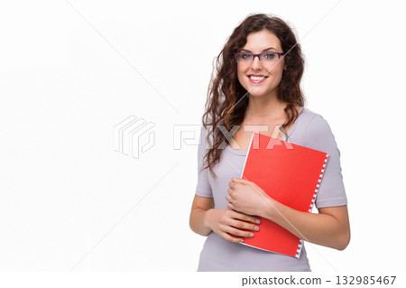 Female student wearing top standing in studio holding red spiral notebook, copy space Female student wearing top standing in studio holding red spiral notebook, copy space 132985467