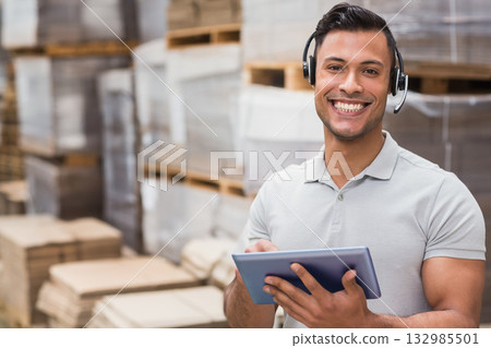 Adult male warehouse worker in grey polo with headset standing by boxes holding tablet, copy space Adult male warehouse worker in grey polo with headset standing by boxes holding tablet, copy space 132985501