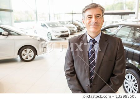 Man standing on tiled floor in car showroom with new sedans and large windows, copy space Man standing on tiled floor in car showroom with new sedans and large windows, copy space 132985503