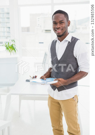 African American man standing holding notebooks, documents at office with monitor and pencil holder African American man standing holding notebooks, documents at office with monitor and pencil holder 132985506