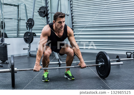 Athletic man squatting with loaded barbell at gym wearing black shoes with green laces beside racks 132985525