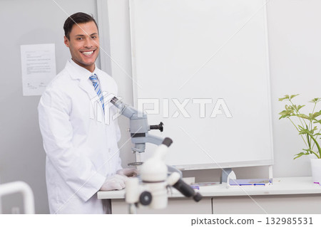 Male researcher standing at lab bench wearing lab coat, gloves operating microscopes, copy space Male researcher standing at lab bench wearing lab coat, gloves operating microscopes, copy space 132985531