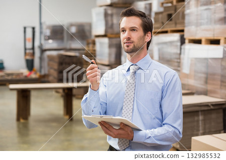 Man in his thirties standing by pallet table inspecting goods on clipboard in warehouse, copy space 132985532